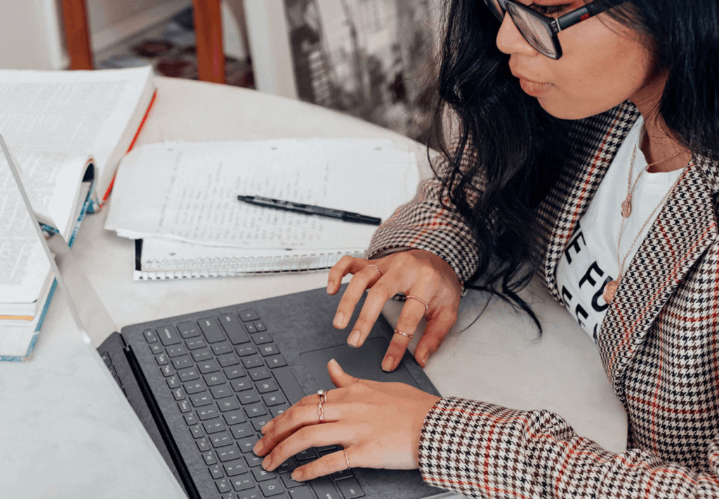 Woman sitting at table with notebooks, typing on laptop