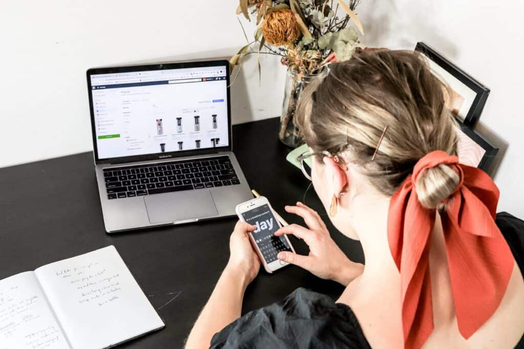 woman using Instagram stories on iPhone while sitting at desk with laptop